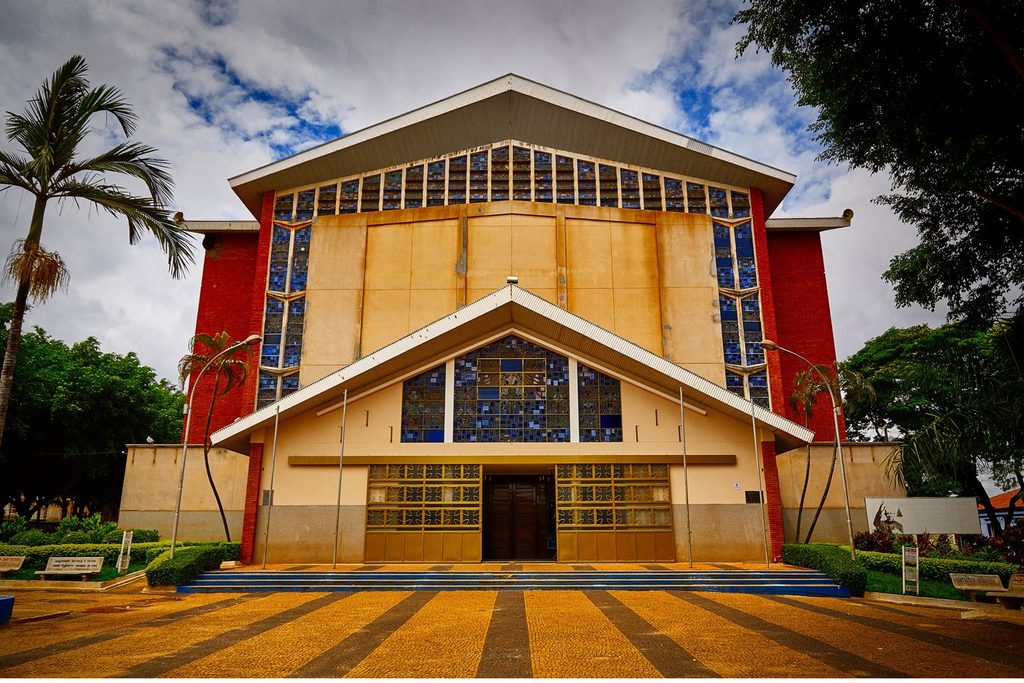 Fachada do Santuário Nossa Senhora Aparecida de Tambaú, com vitrais azuis, paredes vermelhas e praça na frente