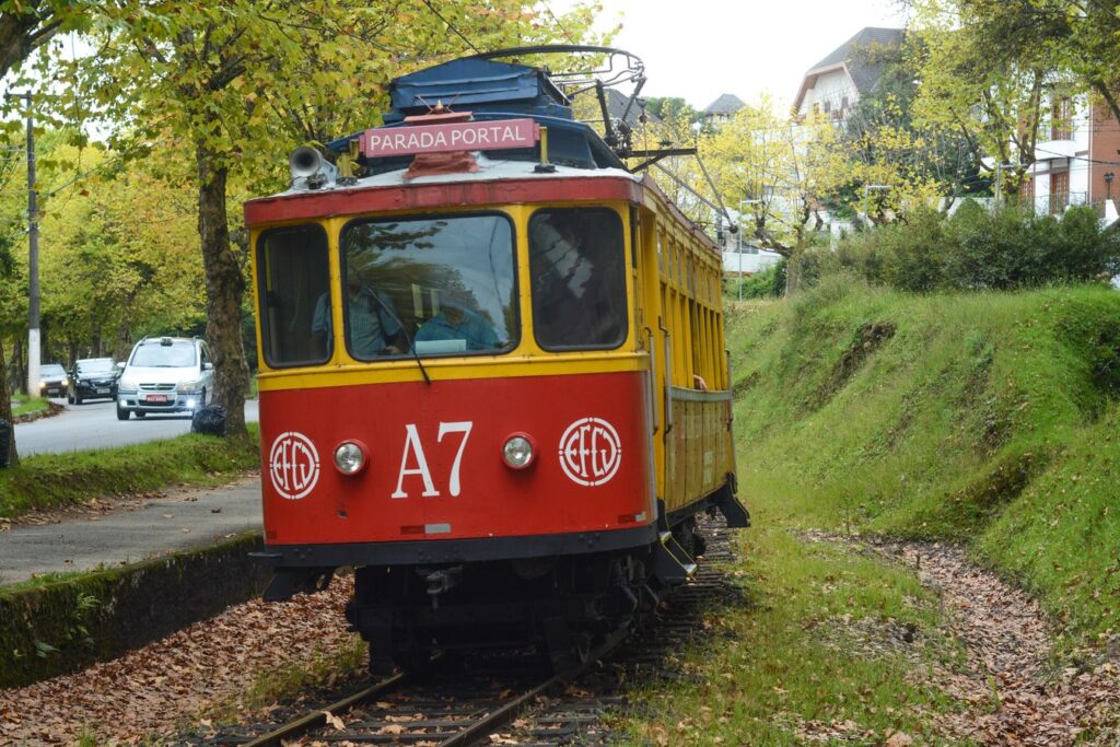 Bondinho A7 vermelho e amarelo do trem de Campos do Jordão parado nos trilhos da Parada Portal, entre árvores
