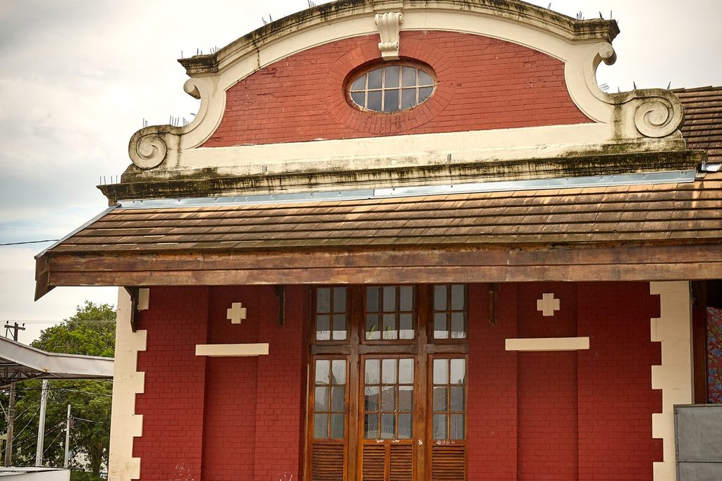 Fachada de tijolos vermelhos com frontão branco ornamentado e portas de madeira da antiga estação ferroviária de Tremembé