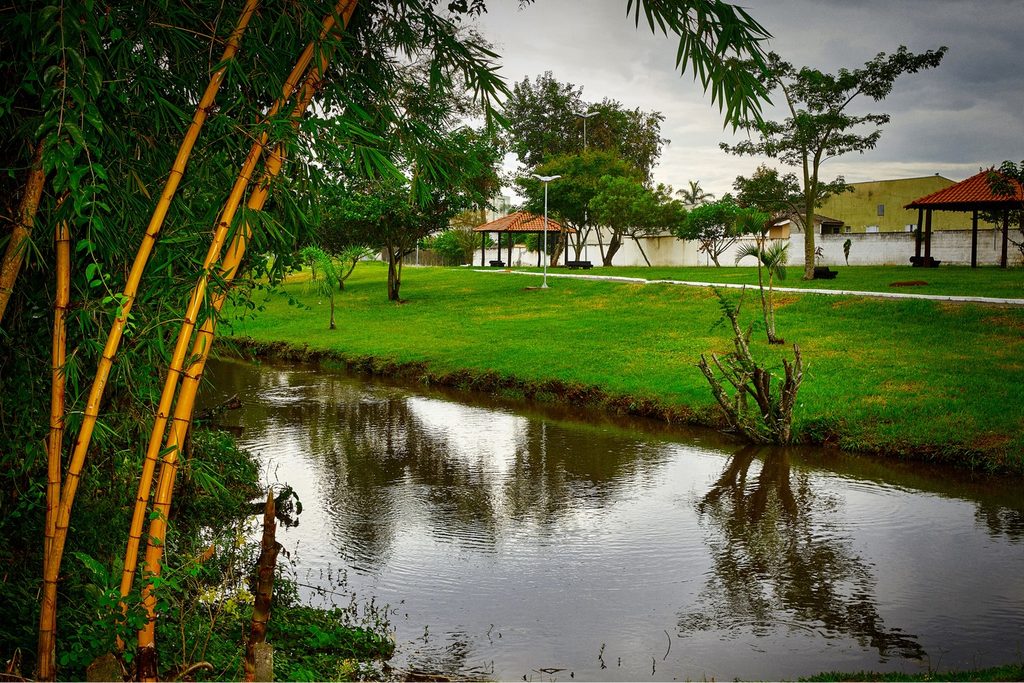 Lago com bambus na margem, gramado e quiosques num parque arborizado