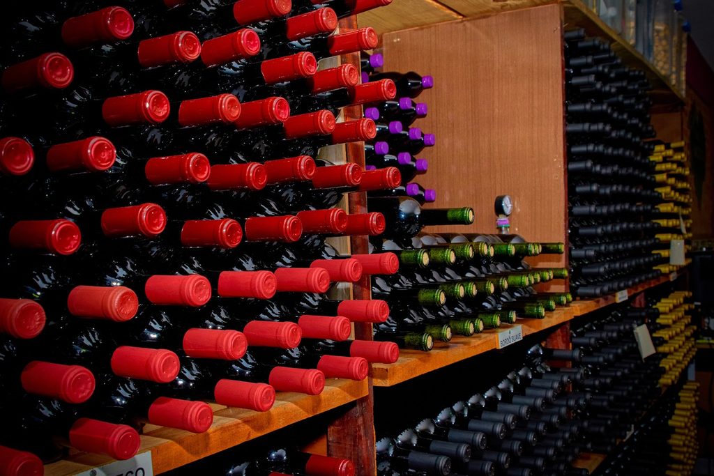 Prateleiras cheias de garrafas de vinho deitadas, com lacres vermelhos, na Adega Família Baccetti, em Vinhedo