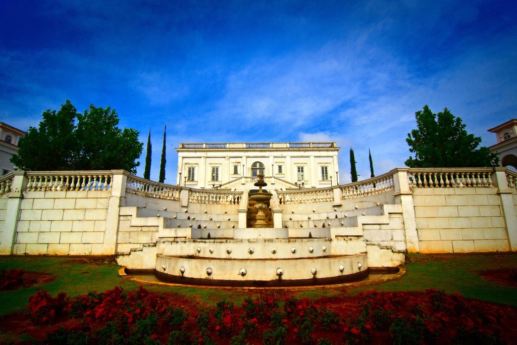 Memorial do Imigrante de Vinhedo, prédio claro em estilo clássico no alto de escadarias com balaustradas, chafariz e canteiro de flores vermelhas